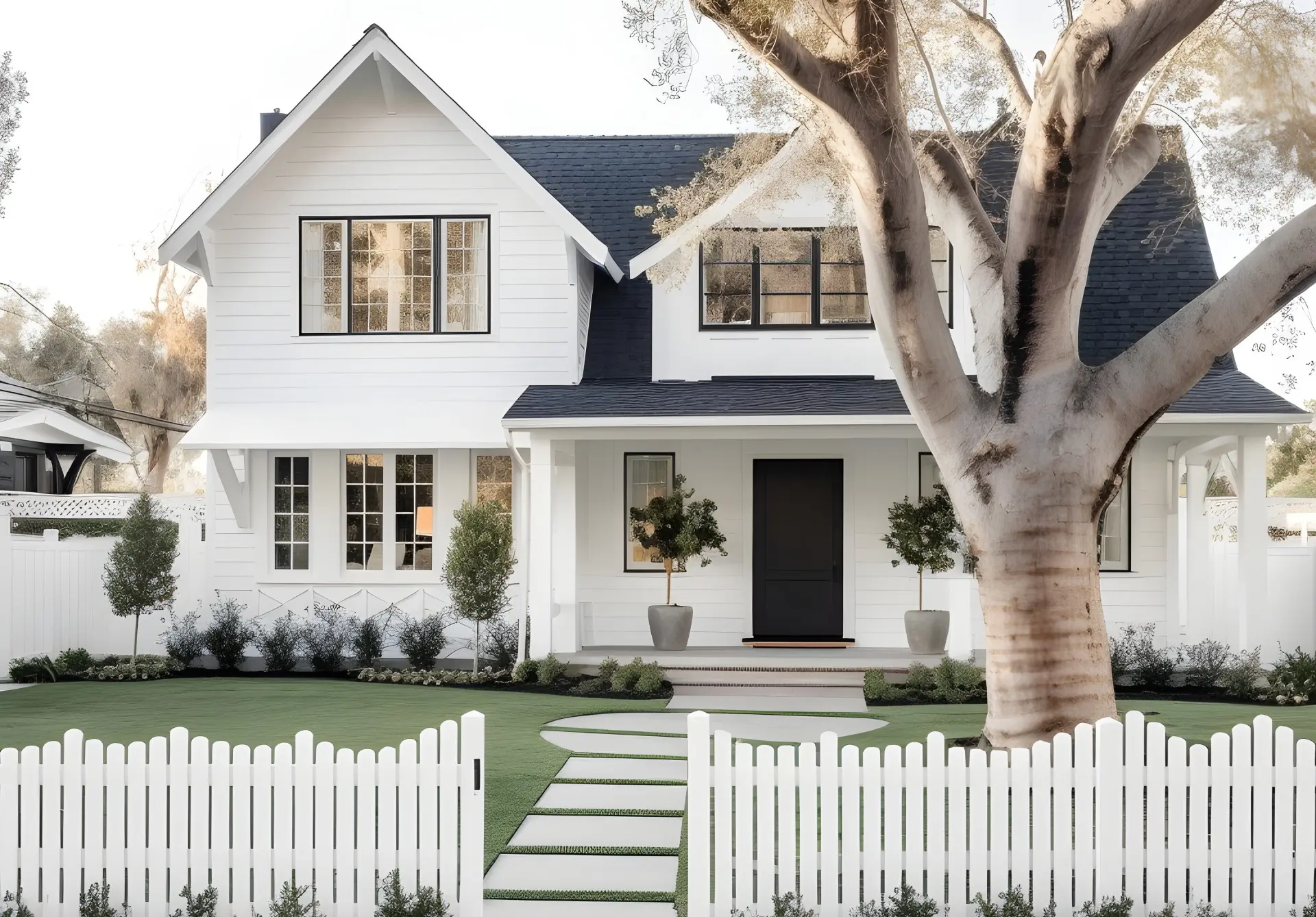 White two-story farmhouse with a dark shingle roof, chimney, front porch, and stone walkway