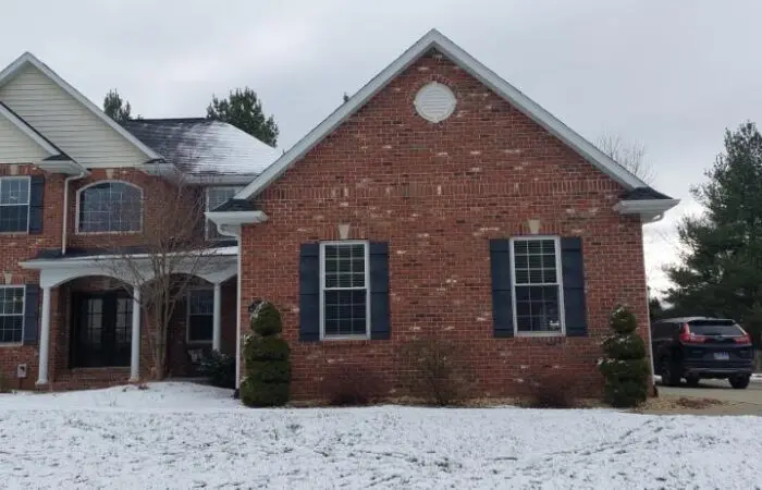 Two-story brick home with black shutters after a snowfall